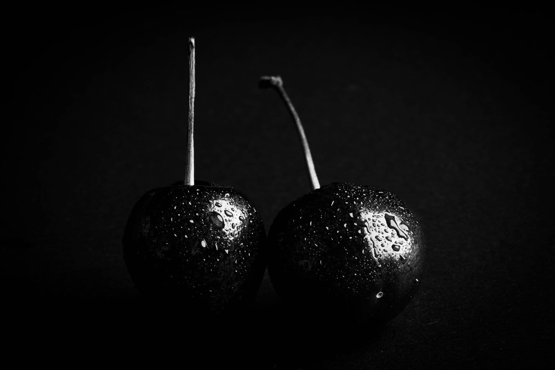 Close-up black and white image of two cherries with water droplets, emphasizing texture and form.