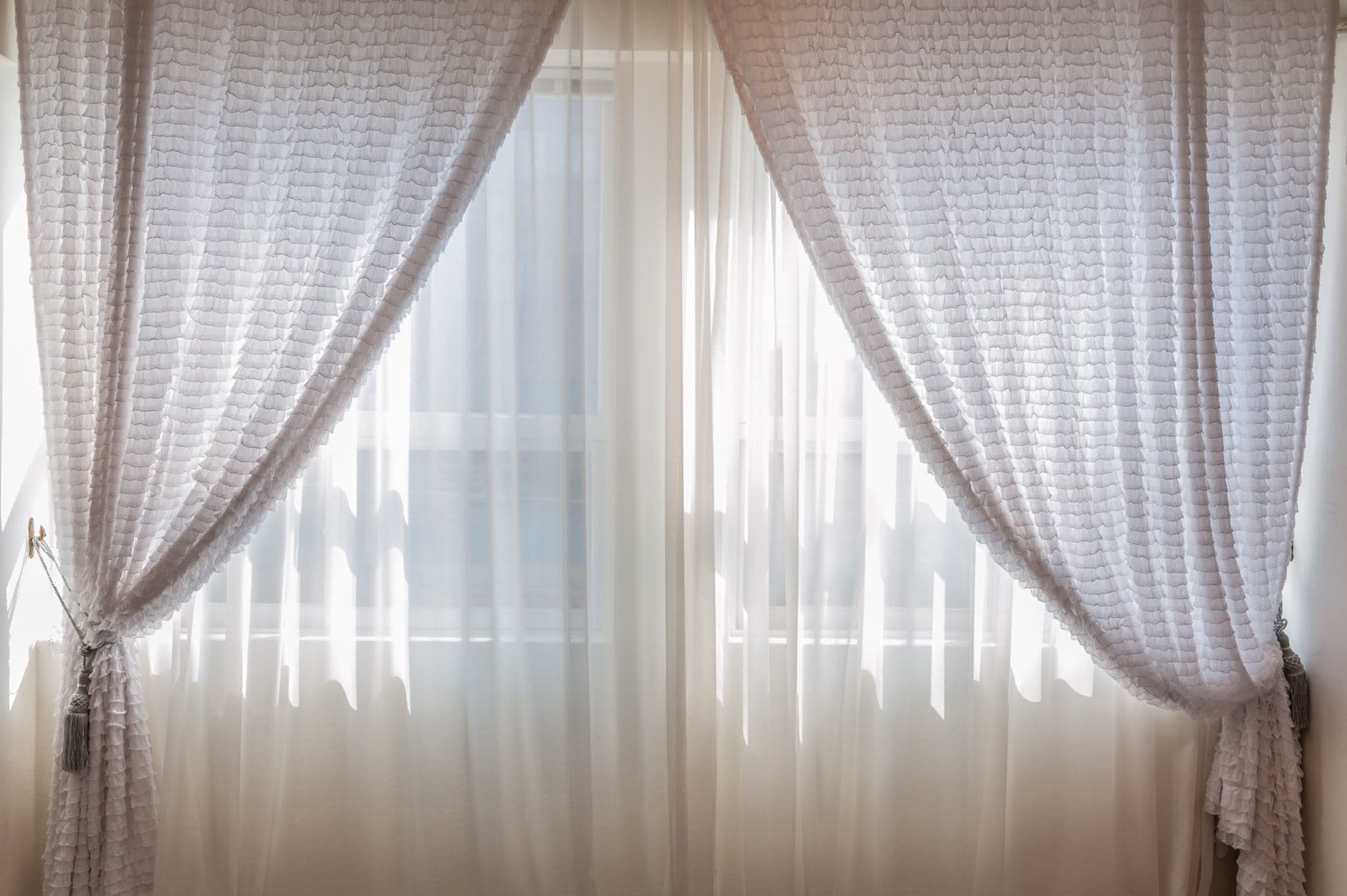 Sheer white curtains drawn back from a bright window