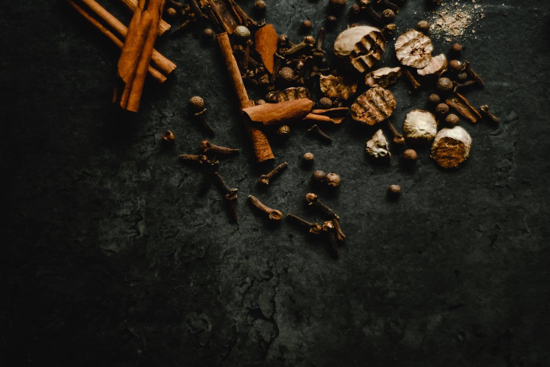 Cinnamon bark, cloves and dried peel scattered across dark stone