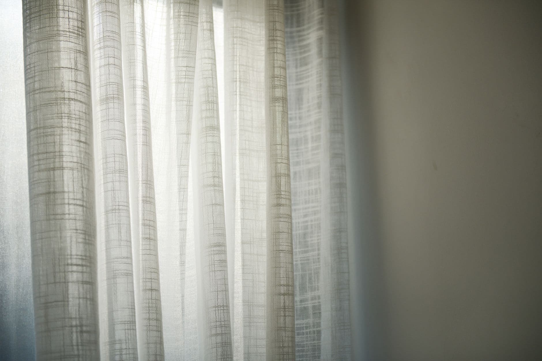 Daylight through a sheer white curtain, casting soft shadows on a wall